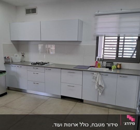 מטבח מאורגן עם ארונות לבנים, כיור וכיריים